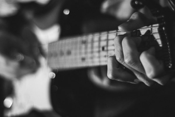 A black and white close up photo of someone playing a Stratocaster.