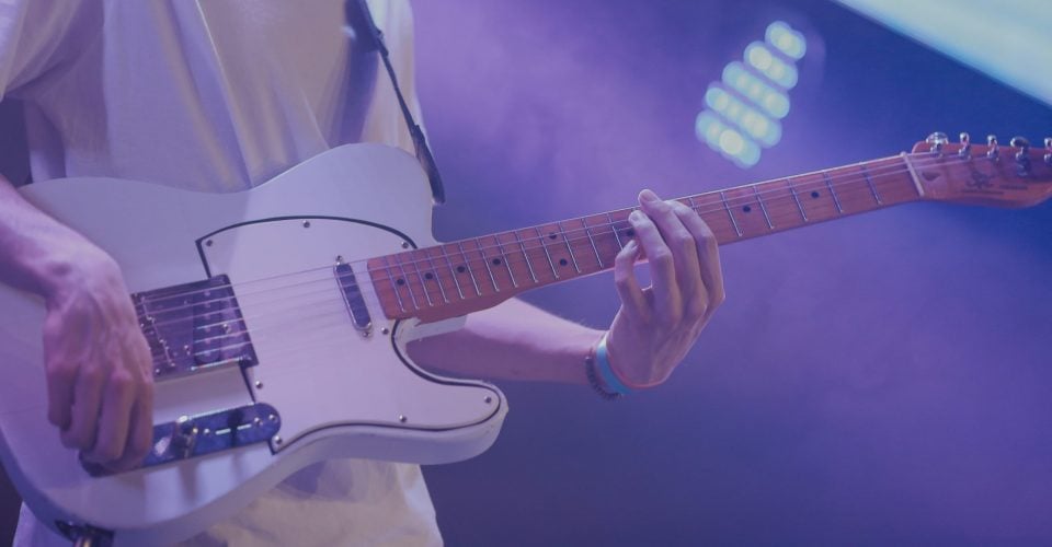 Photo of a man playing a white telecaster on stage.